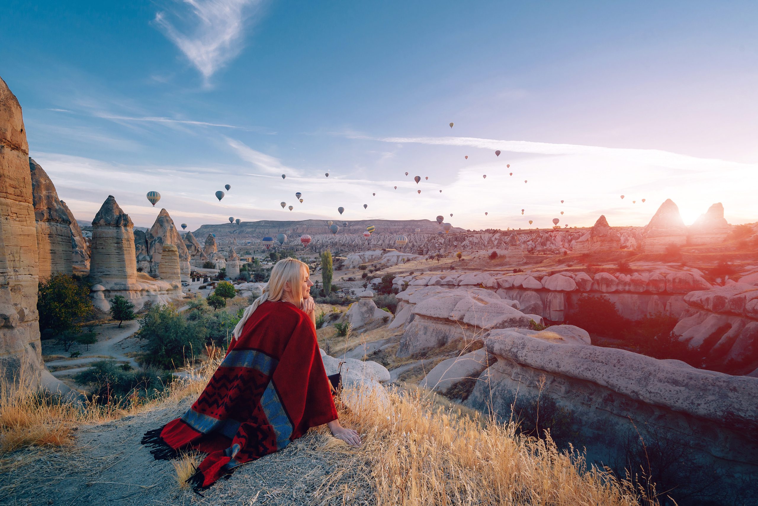 girl in ethnic clothes at dawn watching the flight a lot of balloons fly over the valley of love